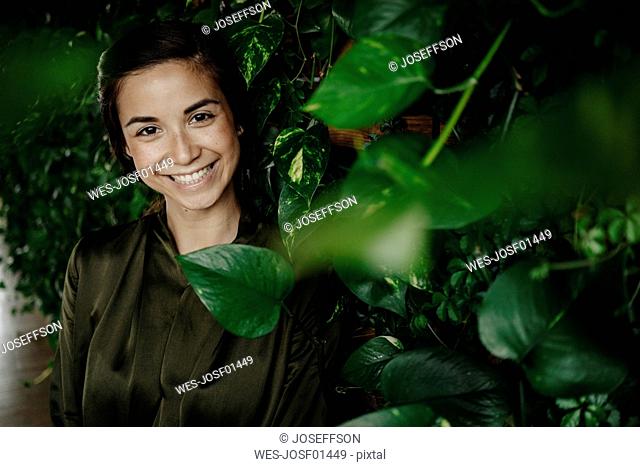 Portait of smiling young woman at wall with climbing plants