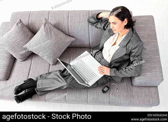 Young businesswoman sitting on sofa, working with laptop computer. Isolated on white background