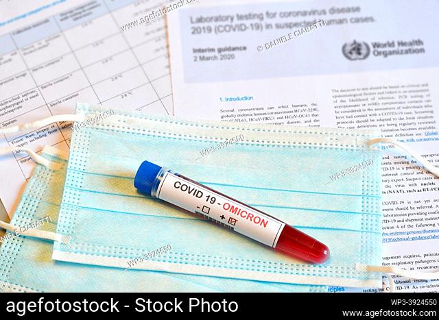 Florence: New Omicron variant of the Covid 19 Virus. Test tube with positive Omicron COVID-19 test blood sample on protective medical masks and documents