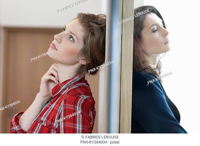 Two female friends standing back to back against a door