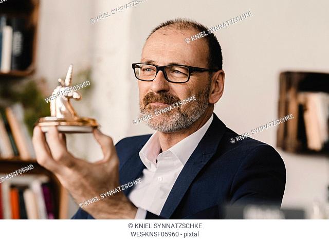 Mature businessman holding a unicorn figurine