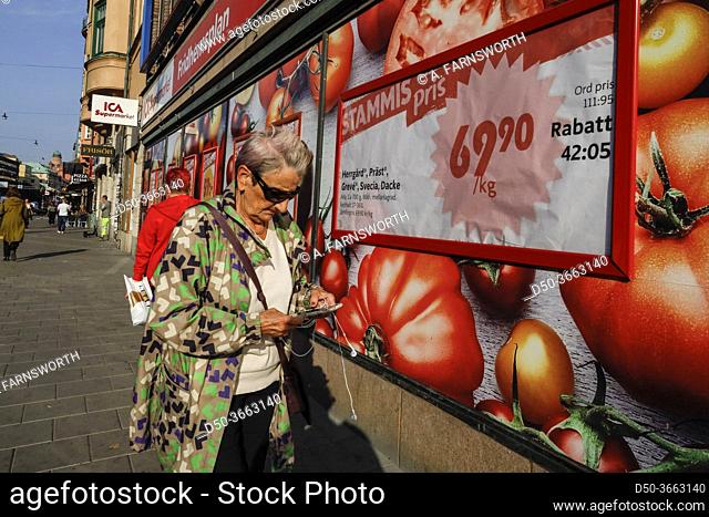 Stockholm, Sweden A senior woman pedestrian on Sankt Eriksgatan on Kungsholmen walks with her phone in front of a supermarket