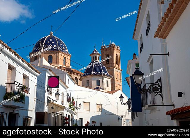 Our Lady of Solace Church with blue tiled domes seen through the sunny alley of the old town of Altea, Costa Blanca, Spain
