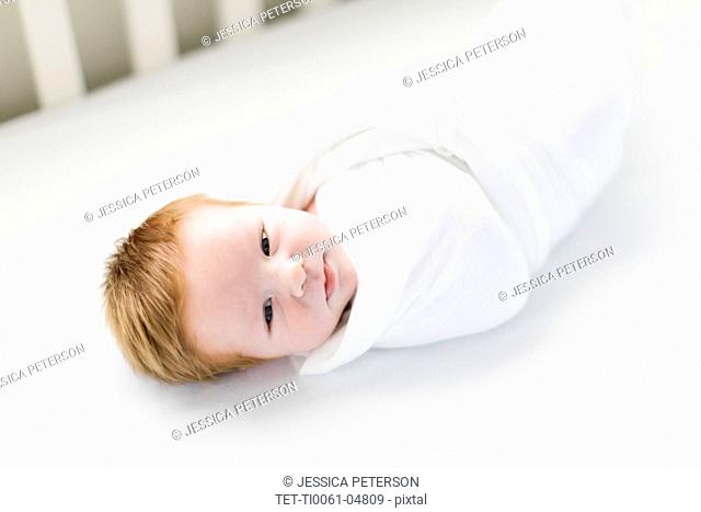 Swaddled baby boy in cot