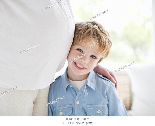 Smiling boy leaning against pregnant mother’s stomach