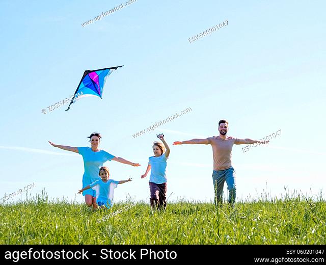 Parents and children running with kite on summer holiday vacation, perfect meadow and sky on seaside