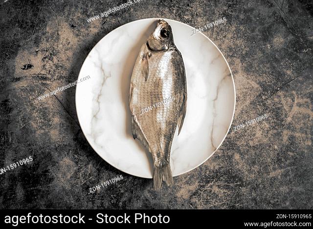 On the plate is salted and dried fish. Presented on a dark background. The view from the top, flat position, copy space