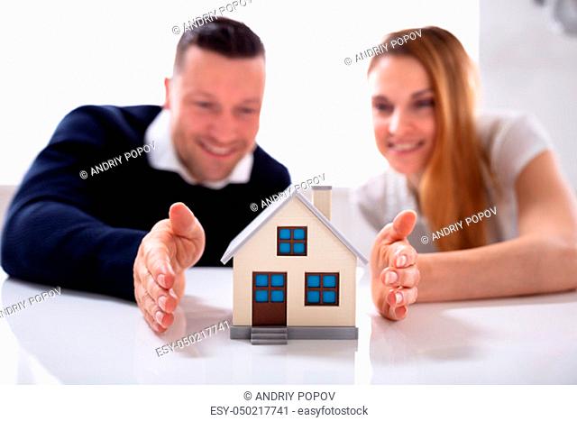Close-up Of Couple's Protecting House Model Over White Desk