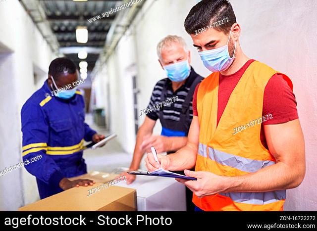 Drei Arbeiter mit Mundschutz wegen Covid-19 kontrollieren Lieferung mit Checkliste