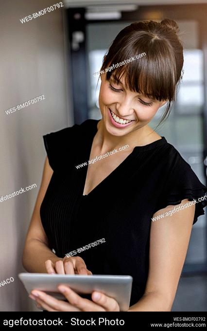 Young smiling businesswoman with bangs using digital tablet in office