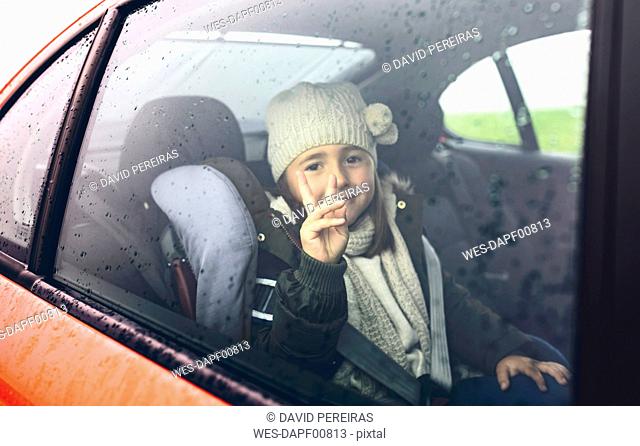 Portrait of happy little girl with wool cap doing victory sign while travelling in car