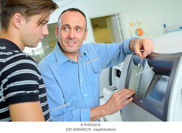 Man showing younger man how to use cash machine