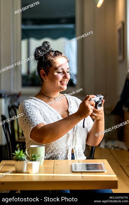 Smiling young woman looking photograph over camera in coffee shop