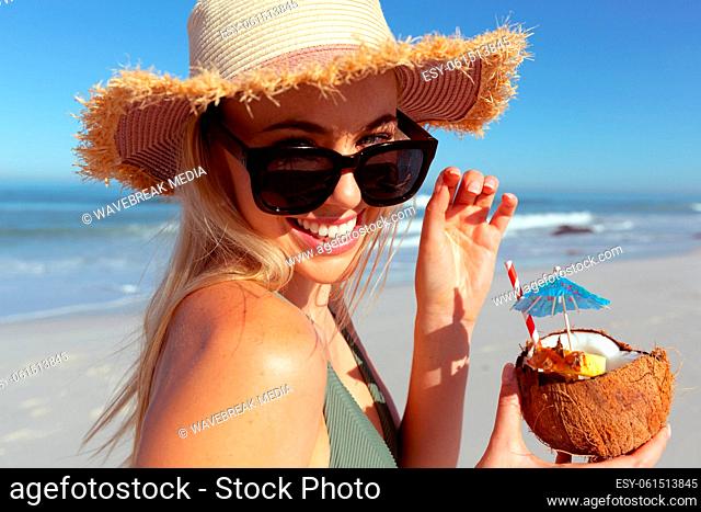 Woman smiling while holding coconut cocktail on the beach