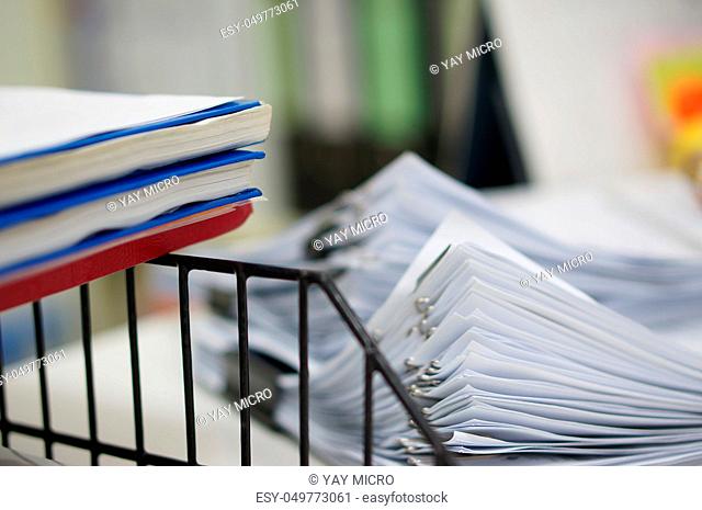 Three of report notebook on black shelf rack and pile of white data papers sheet with clips placed on office desk in the morning at work, office background