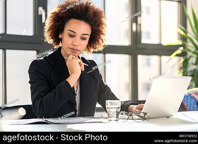 Portrait of African American female expert analyzing printed business report while sitting at desk in the office