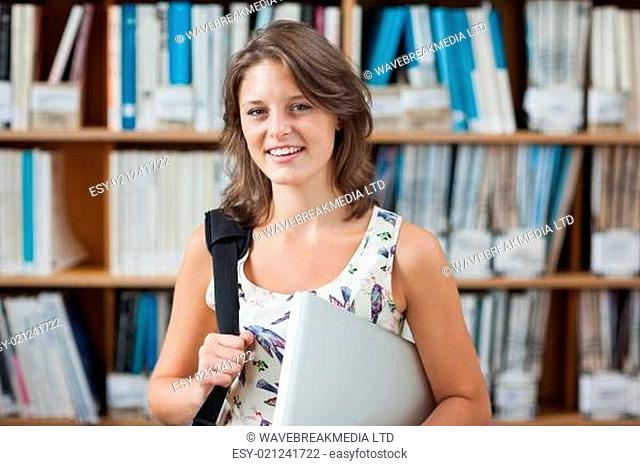Female student against bookshelf with tablet PC and bag in library
