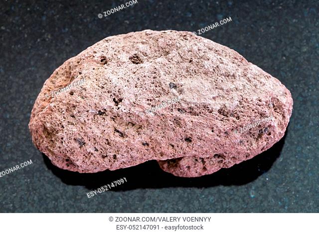 macro shooting of natural mineral rock specimen - red pumice pebble on dark granite background from Sicily