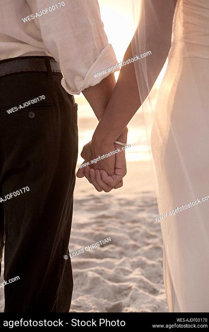 Newlywed couple holding hands while standing at beach