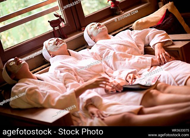 beautiful young women getting facial clay mask at spa, lying with cucumbers on eyes