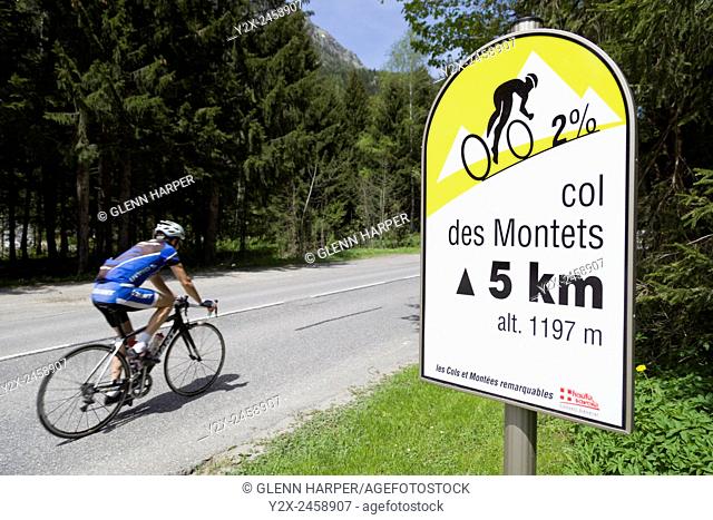A cyclist rides past a sign for the Col des Montets, Haute-Savoie, France; sign shows current gradient and summit altitude
