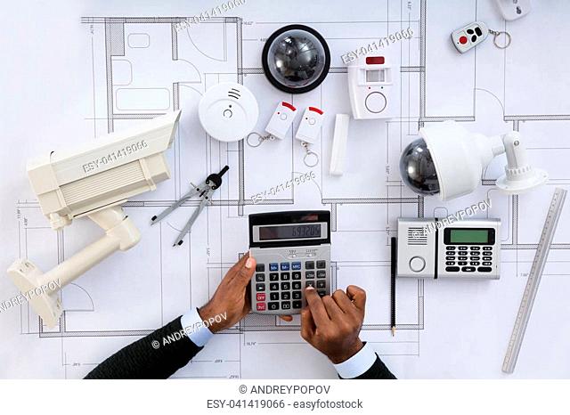 High Angle View Of Architect Hands Using Calculator Working On Blueprint With Security Equipments