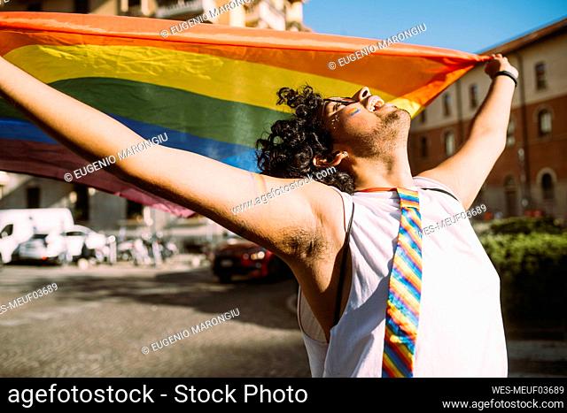 Young male activist looking up while holding rainbow flag on street