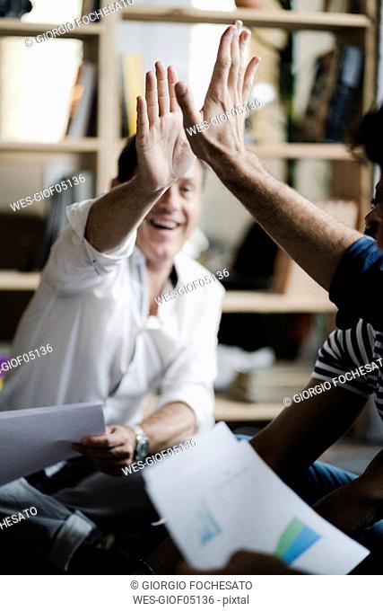 Happy business team sitting on floor with documents high fiving
