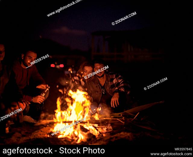 Young Couple Sitting with friends Around Campfire on The Beach At Night drinking beer colored filter
