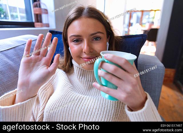 Portrait of woman waving while holding coffee cup