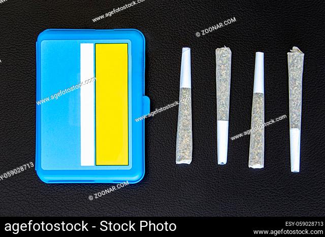 Four Joints of Legal Canadian Cannabis on a black leather background. 2 grams per joint and blue plastic case