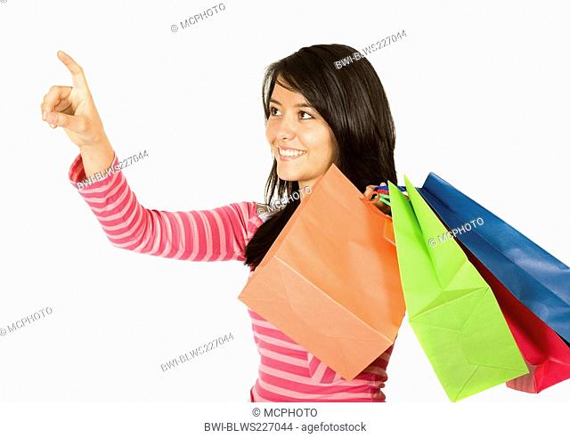 smiling young woman with four shopping bags over her shoulder pointing at the next object of desire