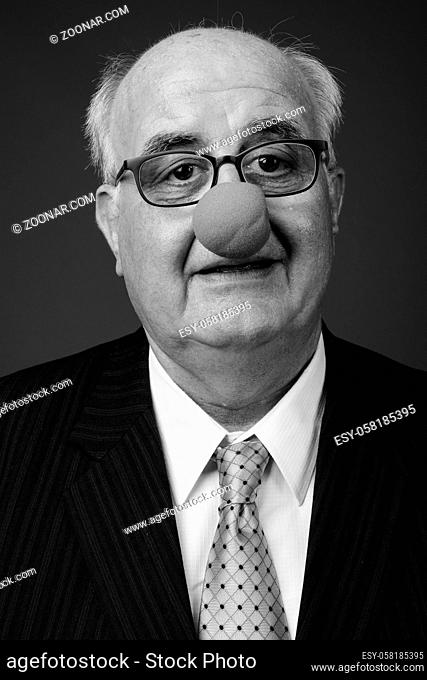 Studio shot of overweight senior businessman wearing clown's nose and eyeglasses against brown background
