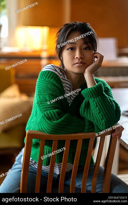 Serious young girl. Asian girl in green shirt at home looking serious