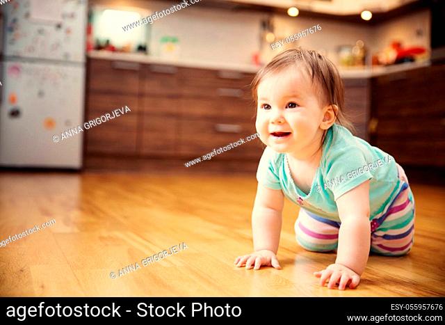 Cute smiling little baby girl crawling on the floor at kitchen. Seven month old infant child at home