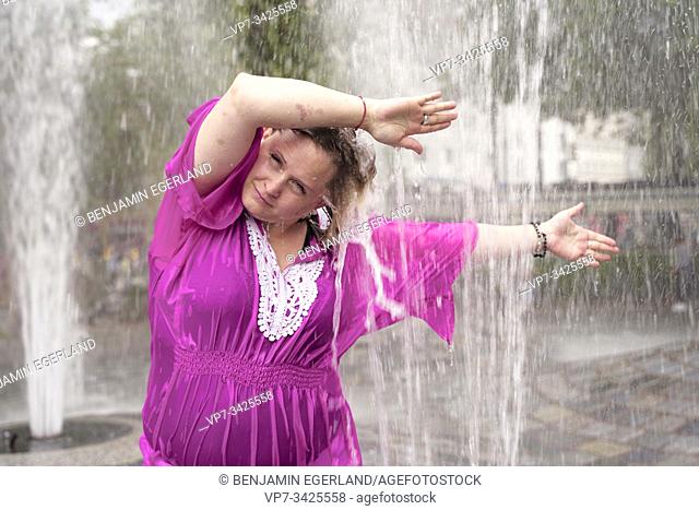 Woman under fountain water spray, Munich, Germany