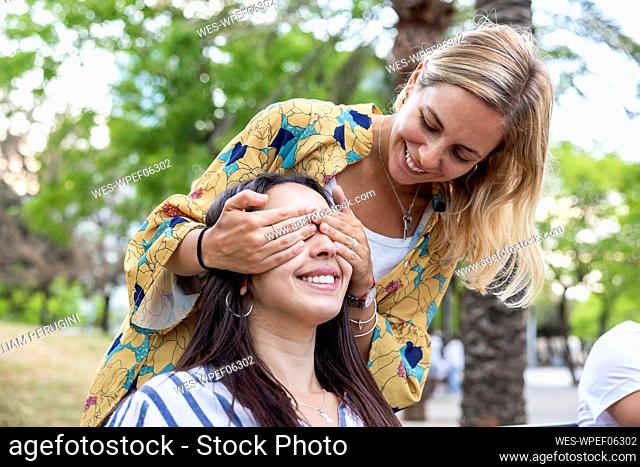 Happy woman covering eyes of friend at park
