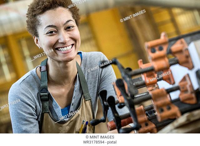 View of a smiling black woman factory worker at her work station in a woodworking factory