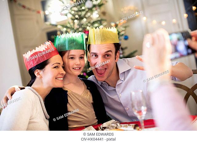 Playful family in paper crowns posing for photograph at Christmas dinner table