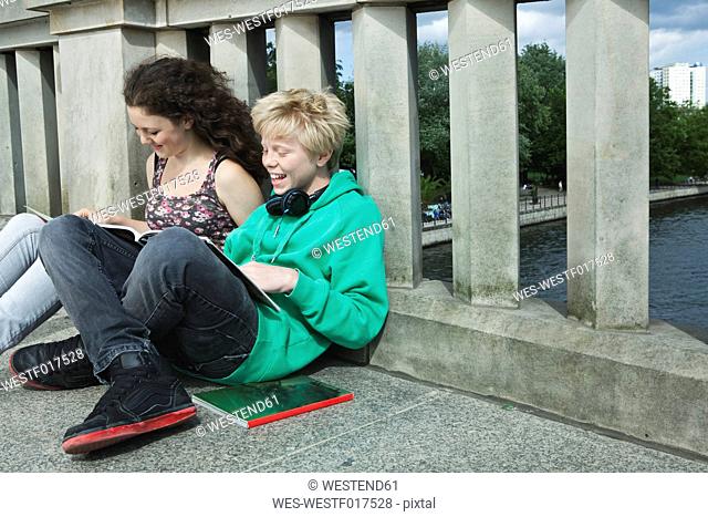 Germany, Berlin, Teenage couple sitting on bridge and reading