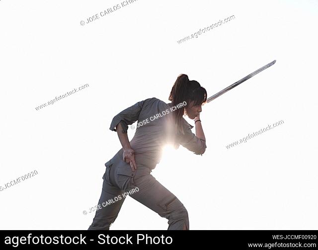 Young woman practicing martial arts with sword on sunny day