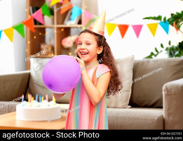 happy girl in birthday party hat blowing balloon