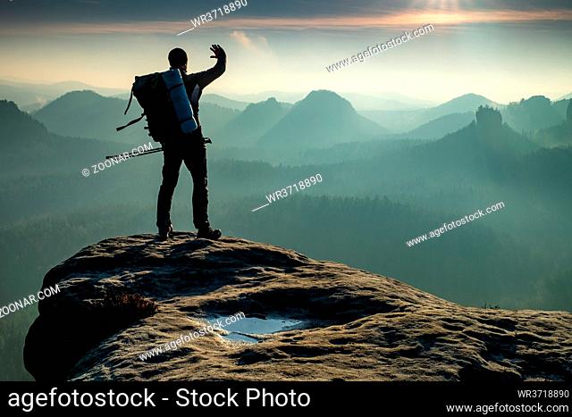 Silhouette of hiker with backpack and walking poles is going in mountains and sunset