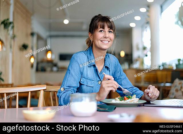 Female owner eating food while sitting in cafe