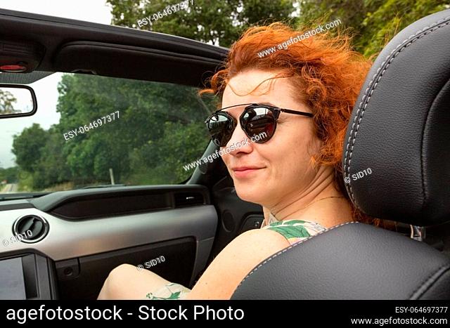 Portrait of beautiful young woman in sunglasses sitting in luxury modern cabriolet car. Portrait happy woman in convertible