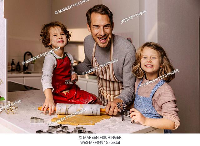 Happy father with two daughters preparing Christmas cookies in kitchen