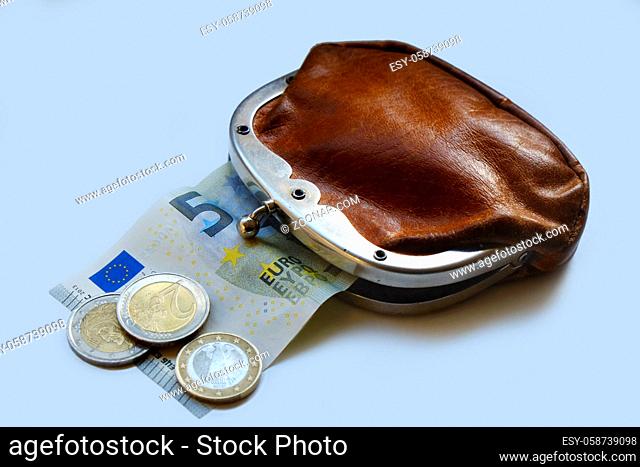 Leicht geoeffnete altmodische Geldboerse aus braunem Leder, aus der ein Geldschein herausragt, davor liegen drei Euro-Muenzen. Freisteller. Querformat