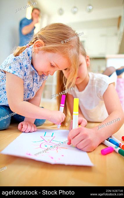 Zwei Kinder malen zusammen ein Bild auf einem Blatt Papier zu Hause