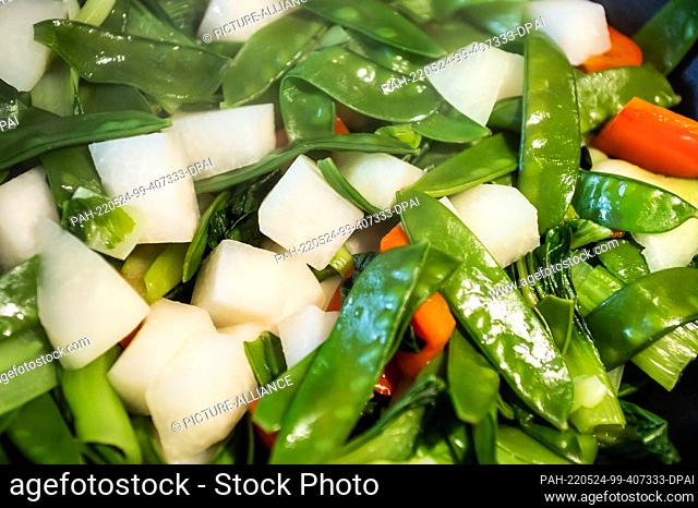 23 May 2022, Baden-Wuerttemberg, Rottweil: Sugar snap peas, red bell peppers, kohlrabi and pak choi are cooked in a wok. Photo: Silas Stein/