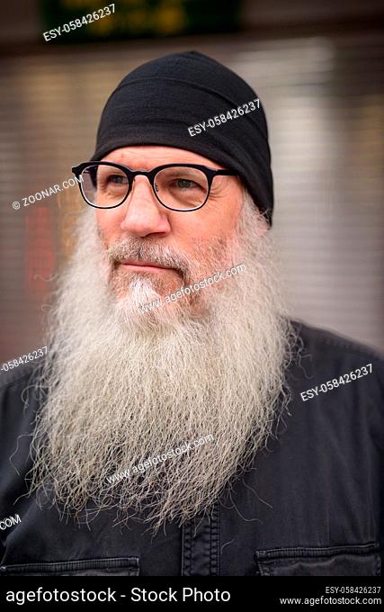 Portrait of mature handsome hipster man with long beard wearing eyeglasses and hat in the streets outdoors